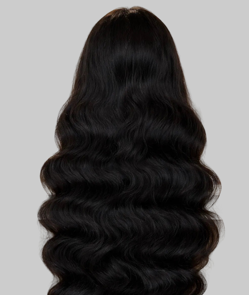 Black hair extensions styled in loose waves with a blurred indoor background