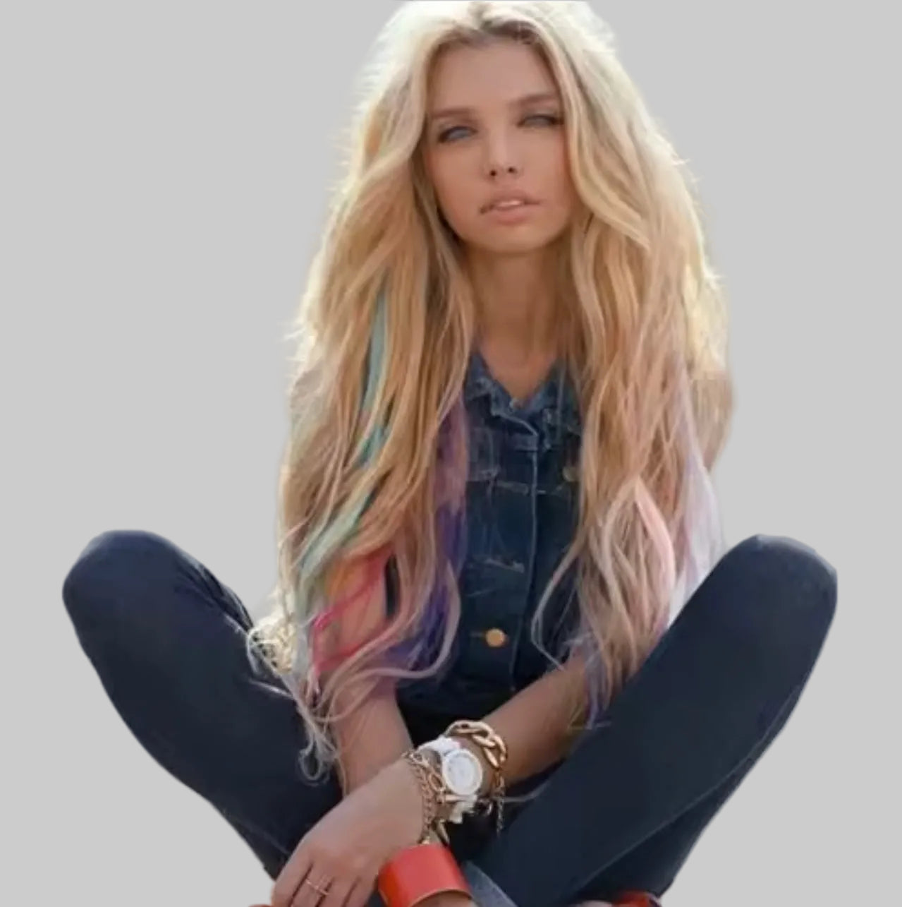 Woman with colorful hair sitting on a bench wearing a denim jacket and dark jeans.
