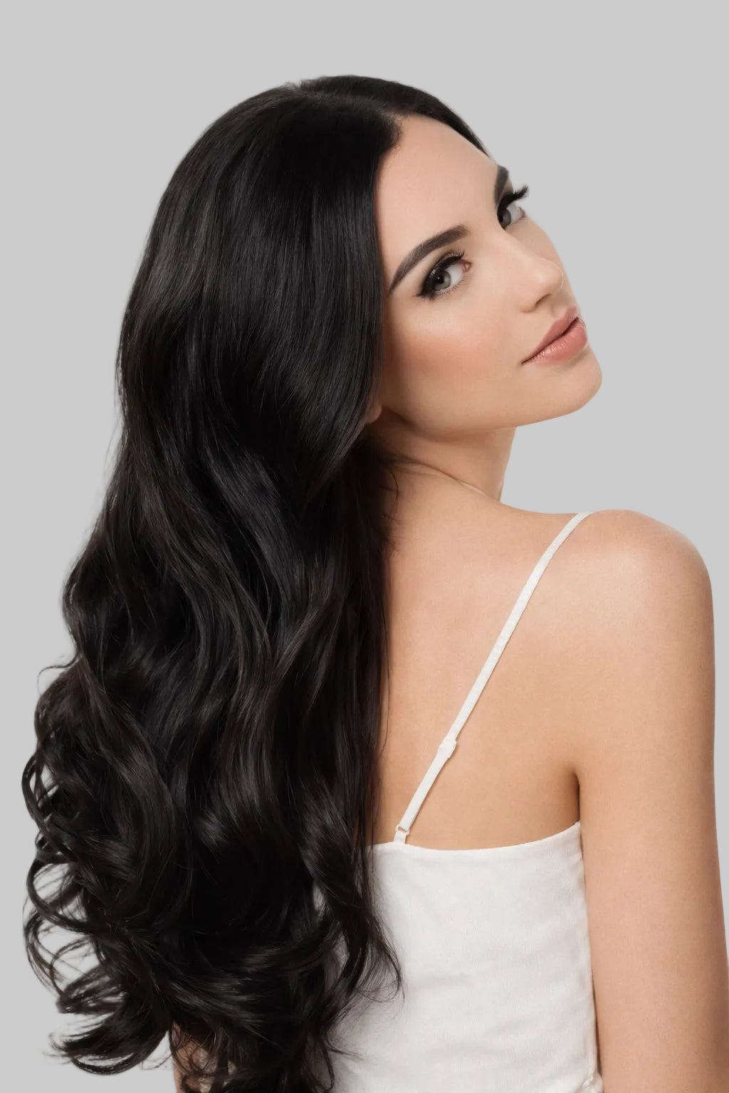 Woman with long, wavy black hair wearing a white top on a white background